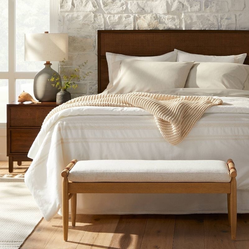 the off white bench with wood legs at the foot of a bed
