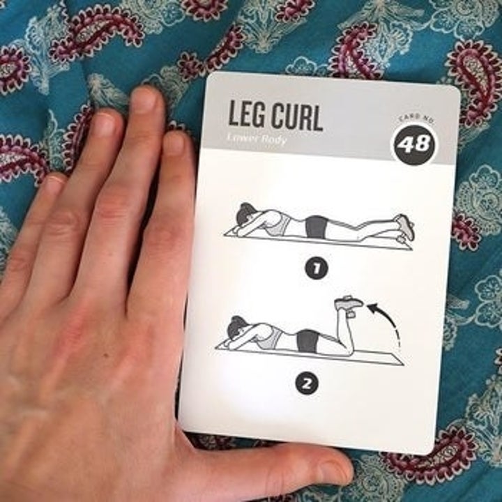 hand holds dumbbell exercise card with illustration of leg curl