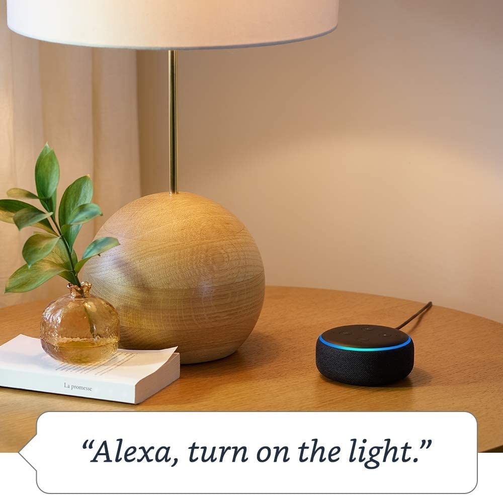 the black hockey puck-shaped Echo Dot on a table with the command, &quot;Alexa, turn on the light&quot; written on the image