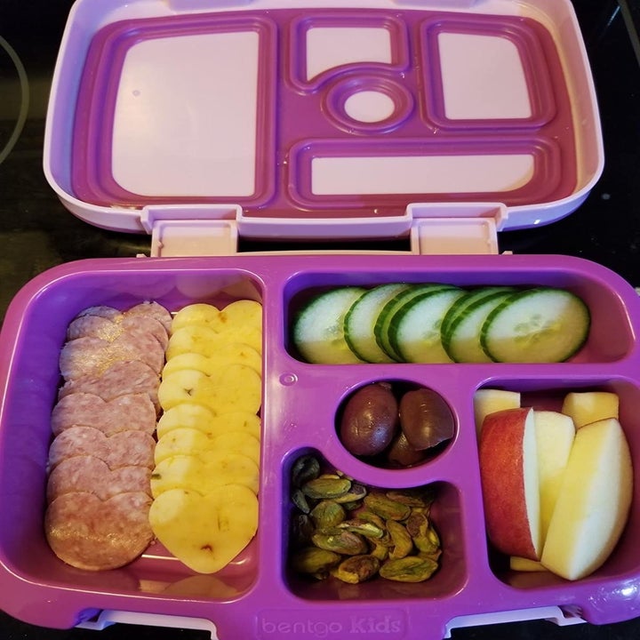 a purple lunchbox with heart-shaped slices of meat and cheese, cucumbers, apple slices, olives, and nuts