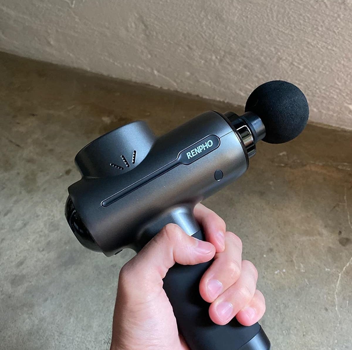 A person holding the handle of a black massage gun