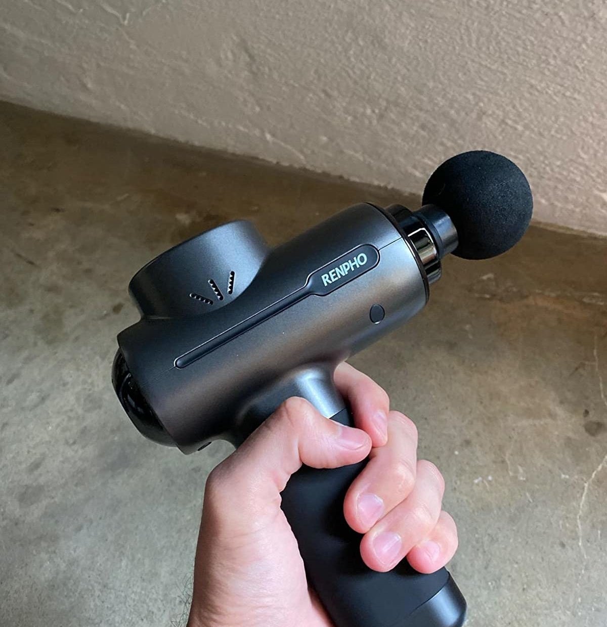 A person holding the handle of a black massage gun