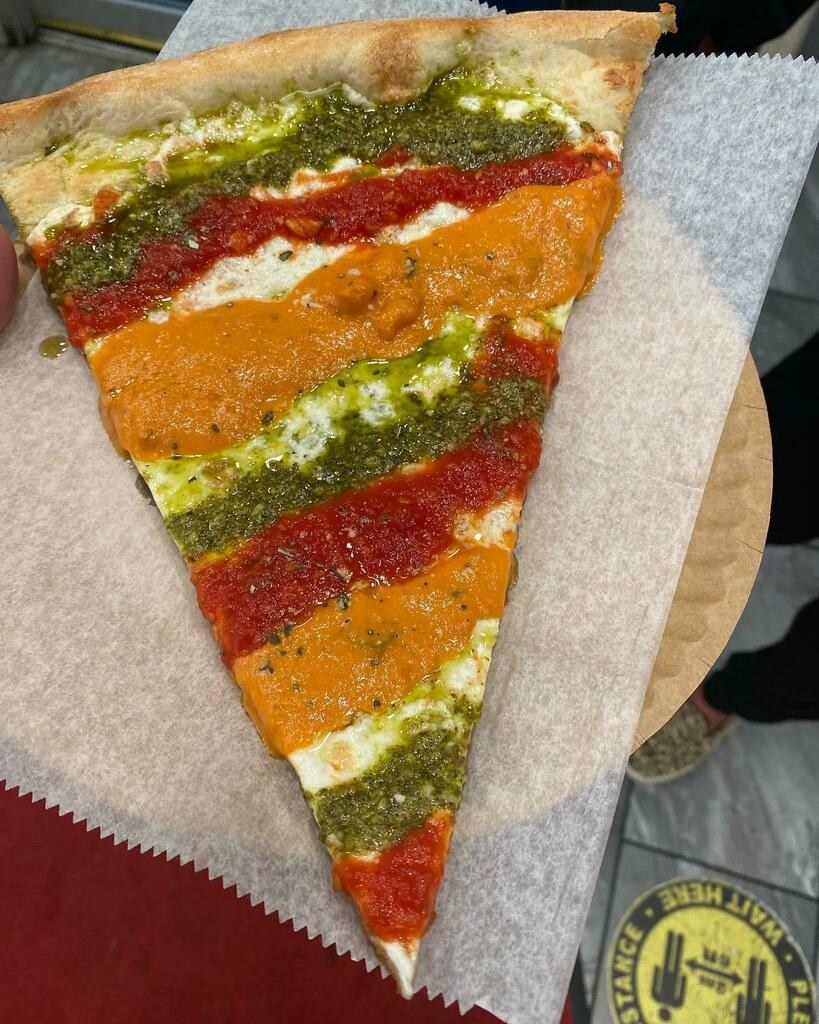 A slice of pizza topped with pesto, marinara sauce, and vodka sauce.