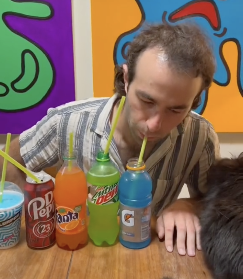 A series of five drinks are set up in front of Davey, all with straws coming out of them; Davey is drinking out of a bottle with blue Gatorade