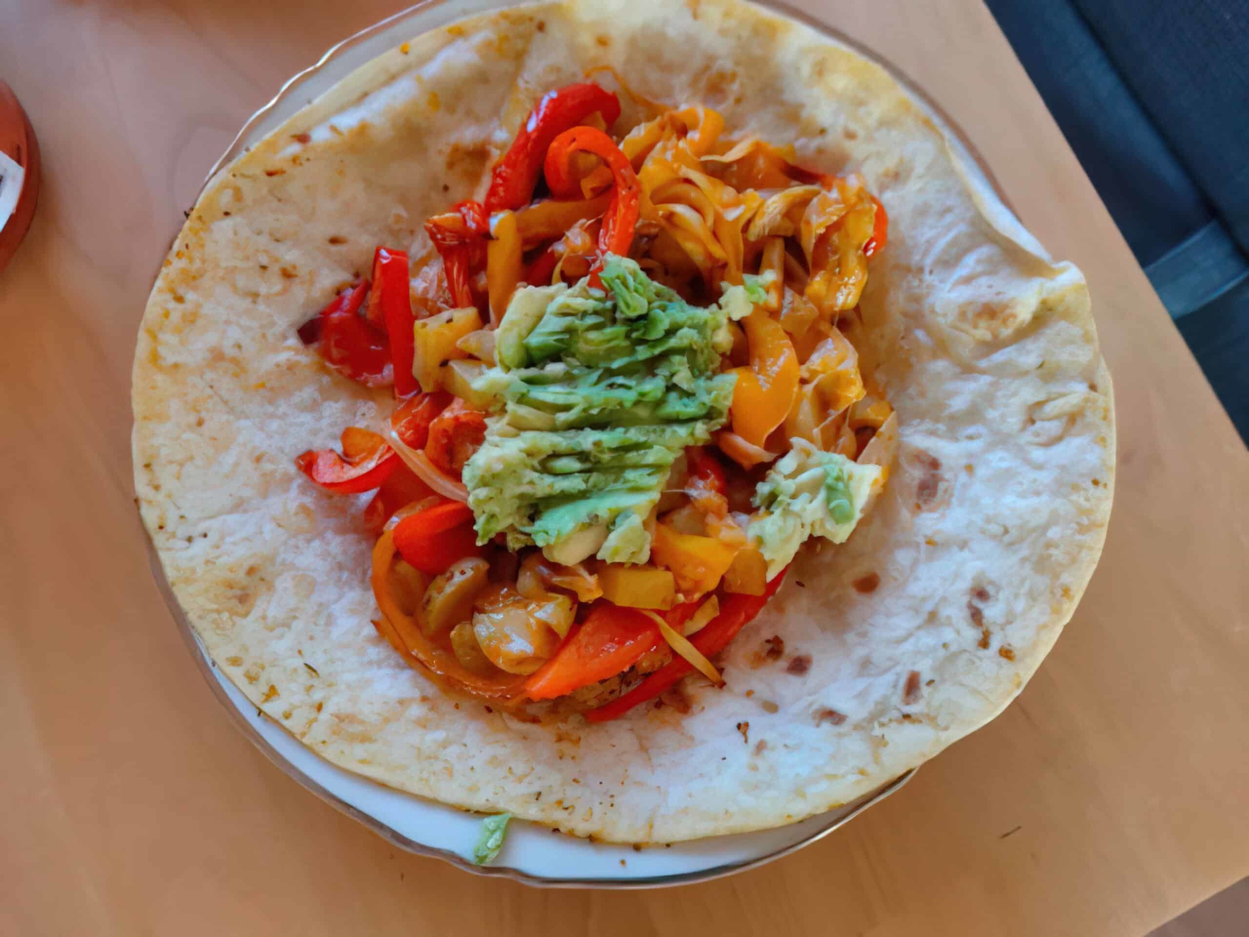 A tortilla topped with grilled potatoes, peppers, onion, and guacamole.