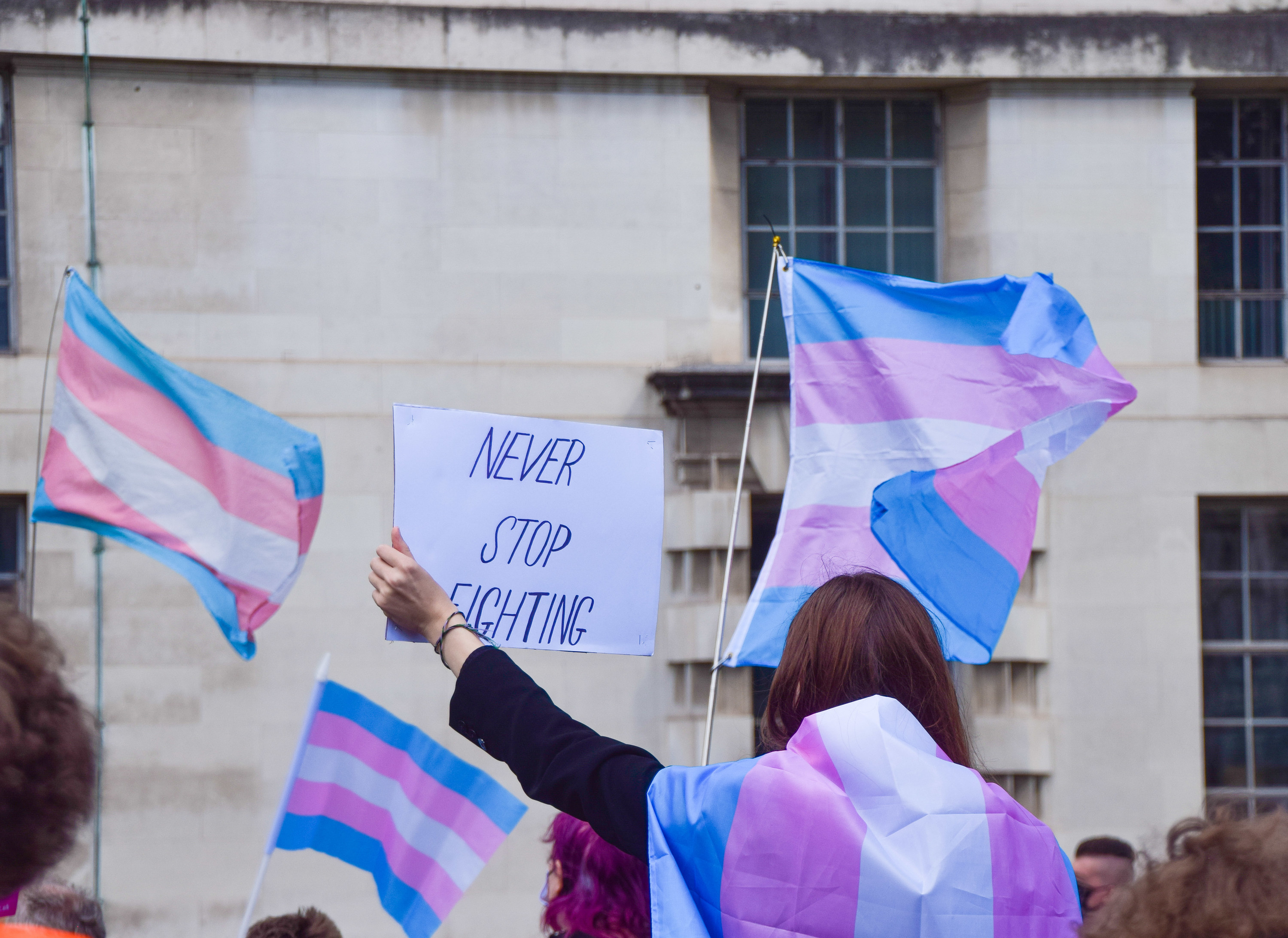 protestors with trans flags and a sign that says never stop fighting