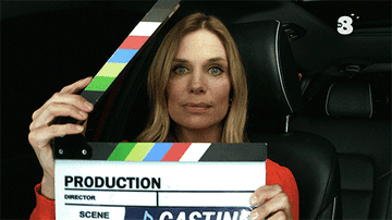 A woman claps a movie slate while sitting in a car