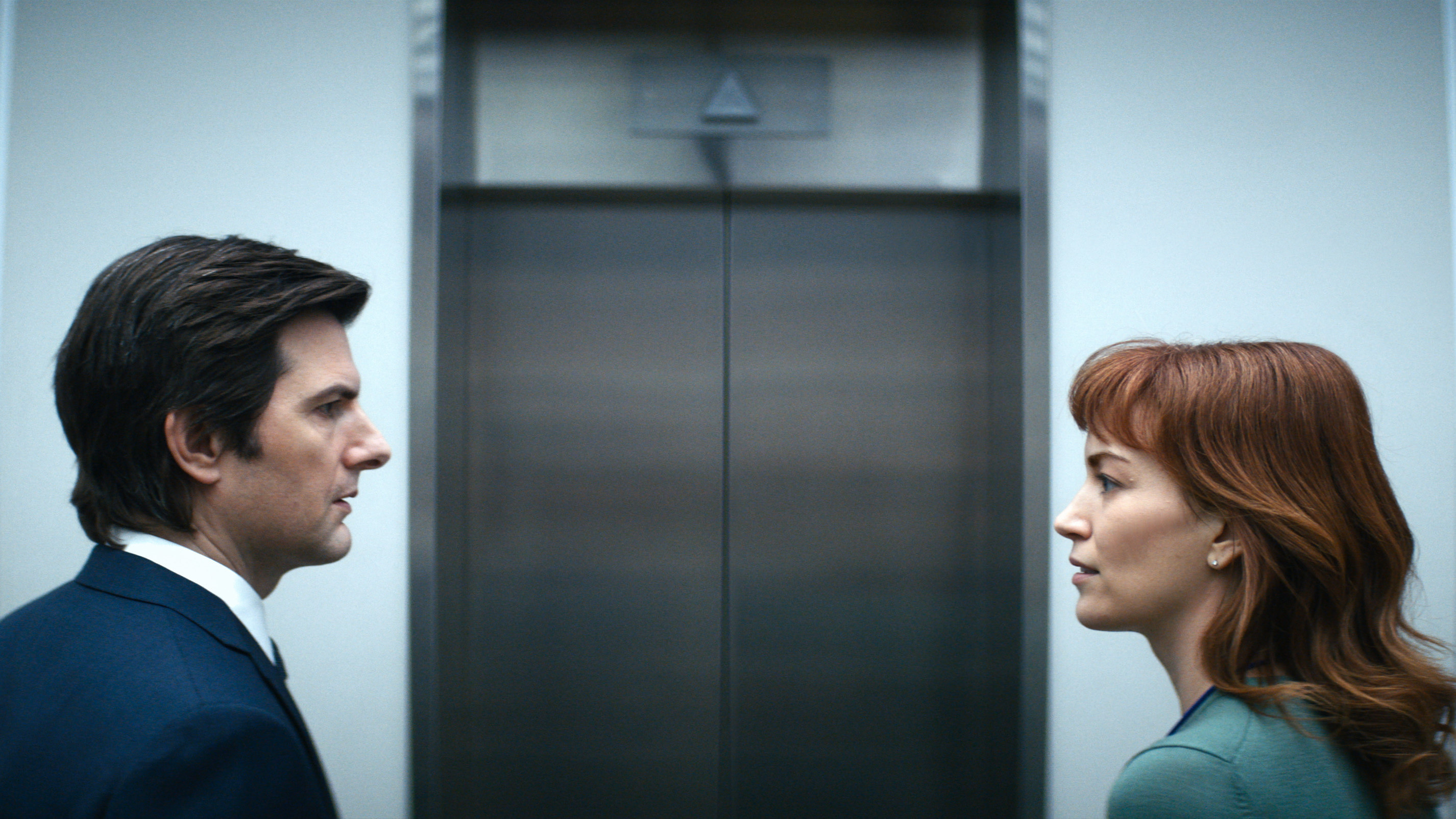 Adam Scott and Britt Lower look at one another near an elevator