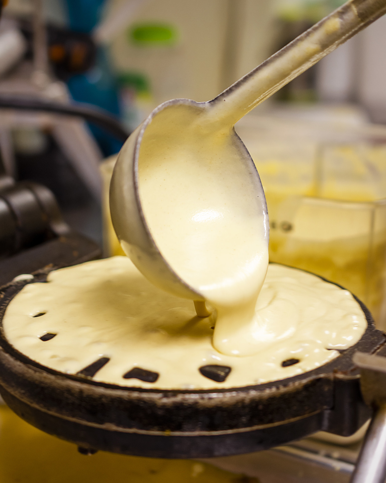 Waffle batter being poured into a waffle iron with a ladle.