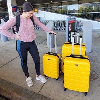 person standing next to three yellow suitcases in different sizes