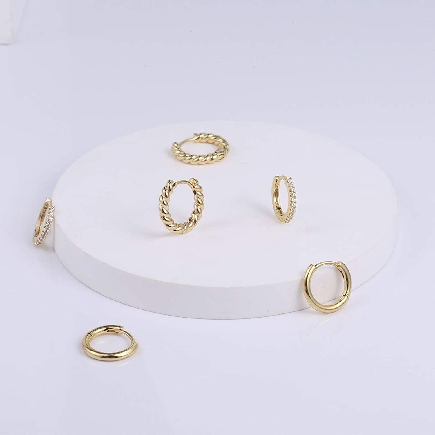 Three sets of huggie hoop earrings against a circular piece on top of a counter