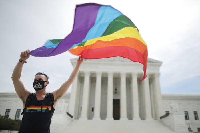 A person holds a rainbow pride flag in front of the Supreme Court