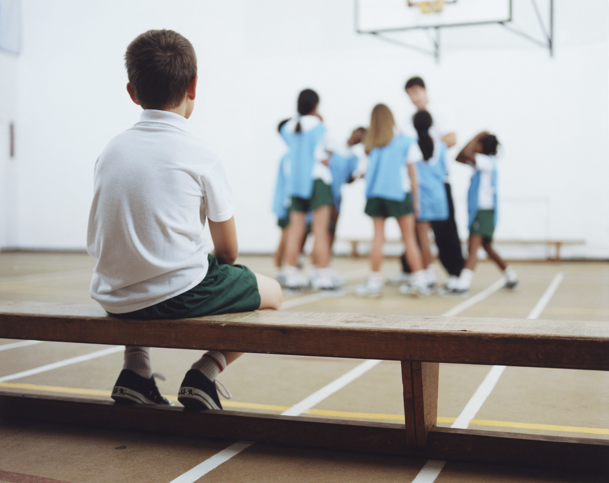 a kid sitting on the bleachers while a team of kids talks to a coach in a gym