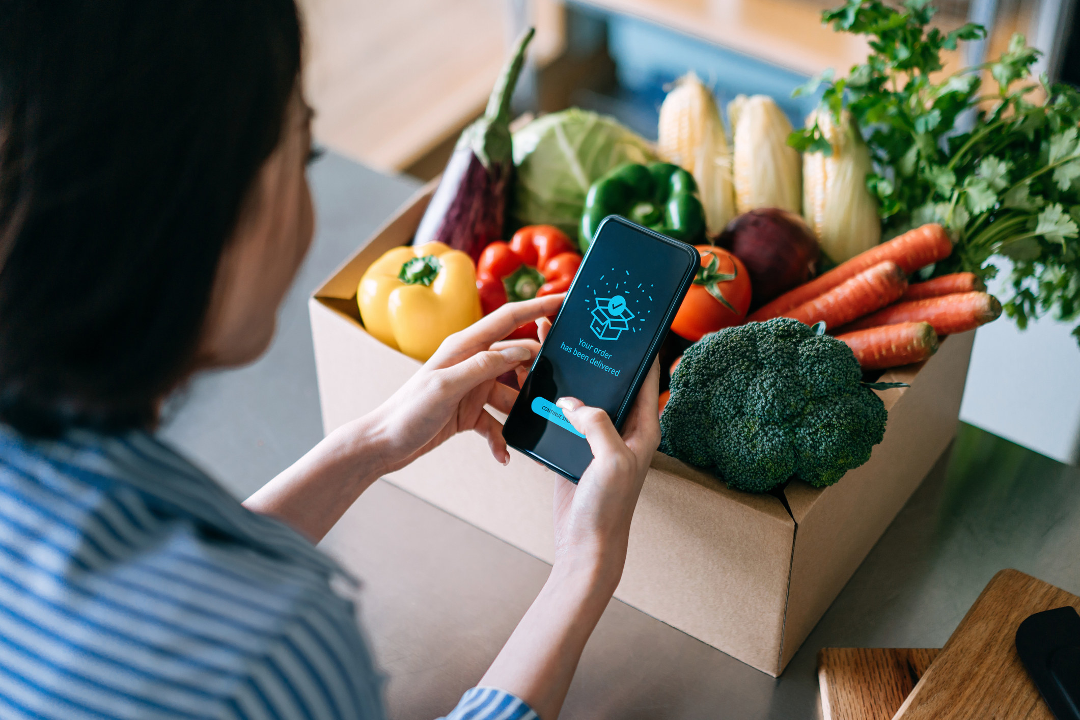 A person opens an app while looking at a box of vegetables