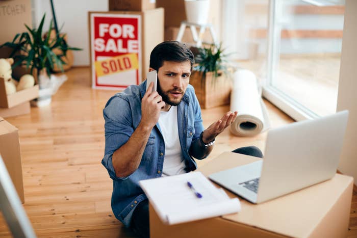 A man sitting on the floor next to boxes looking confused