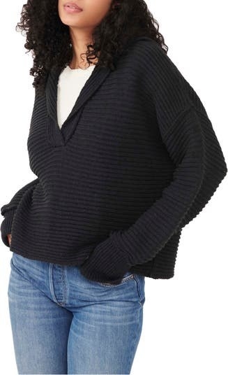 Model wearing black knit pullover sweater with jeans and white shirt underneath