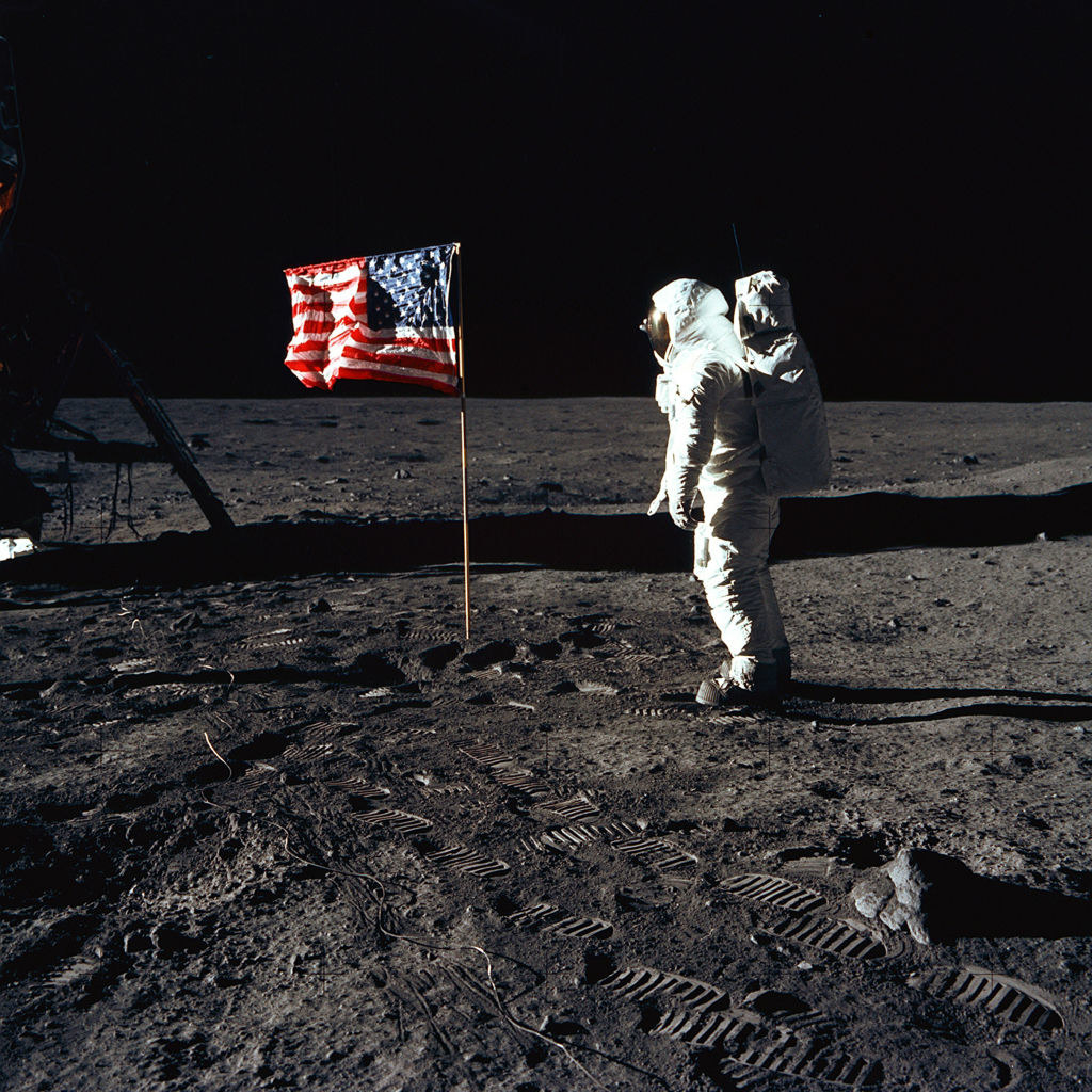 astronaut standing and looking at the flag on the moon