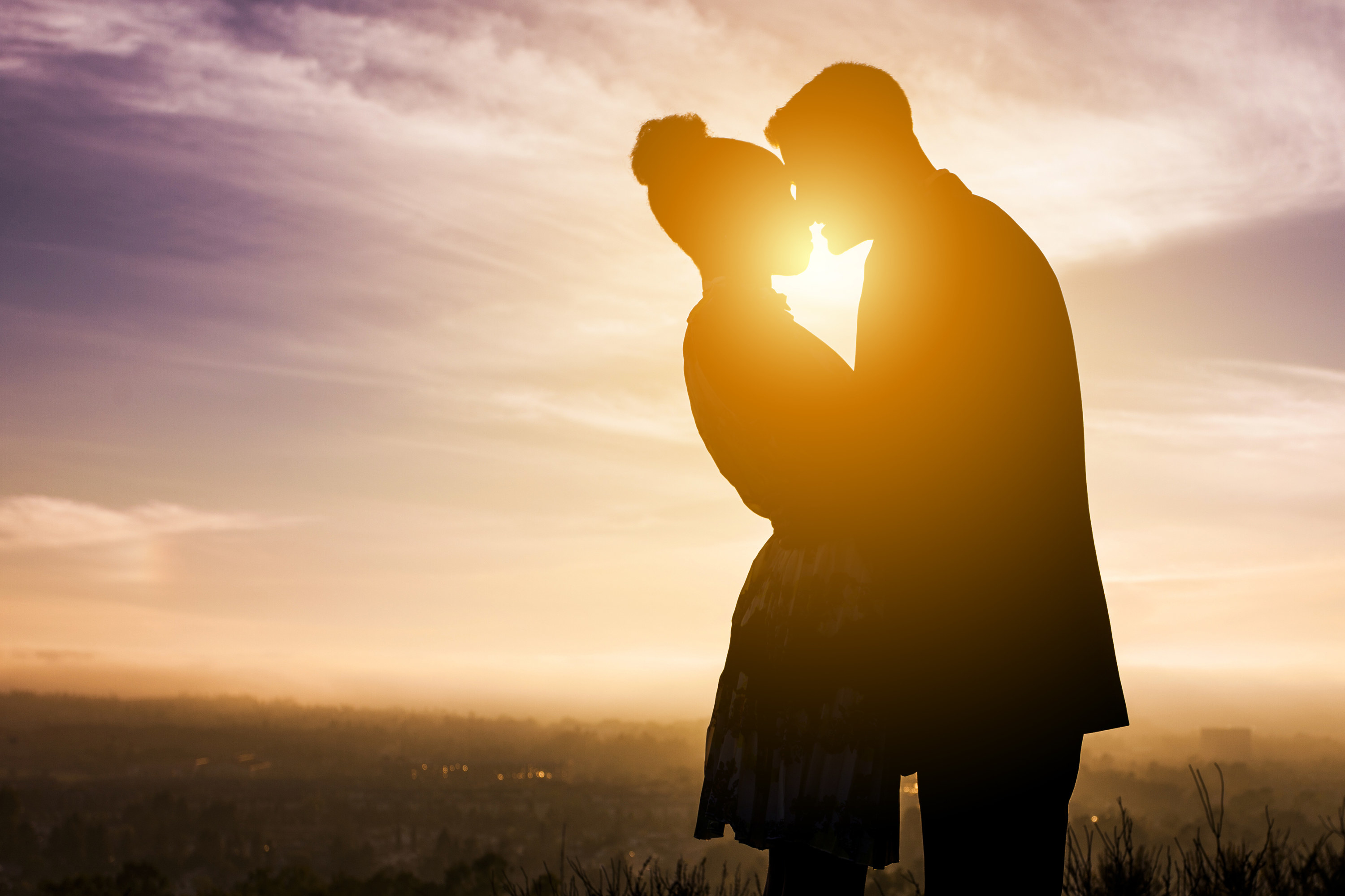 A couple kisses in front of a sunset