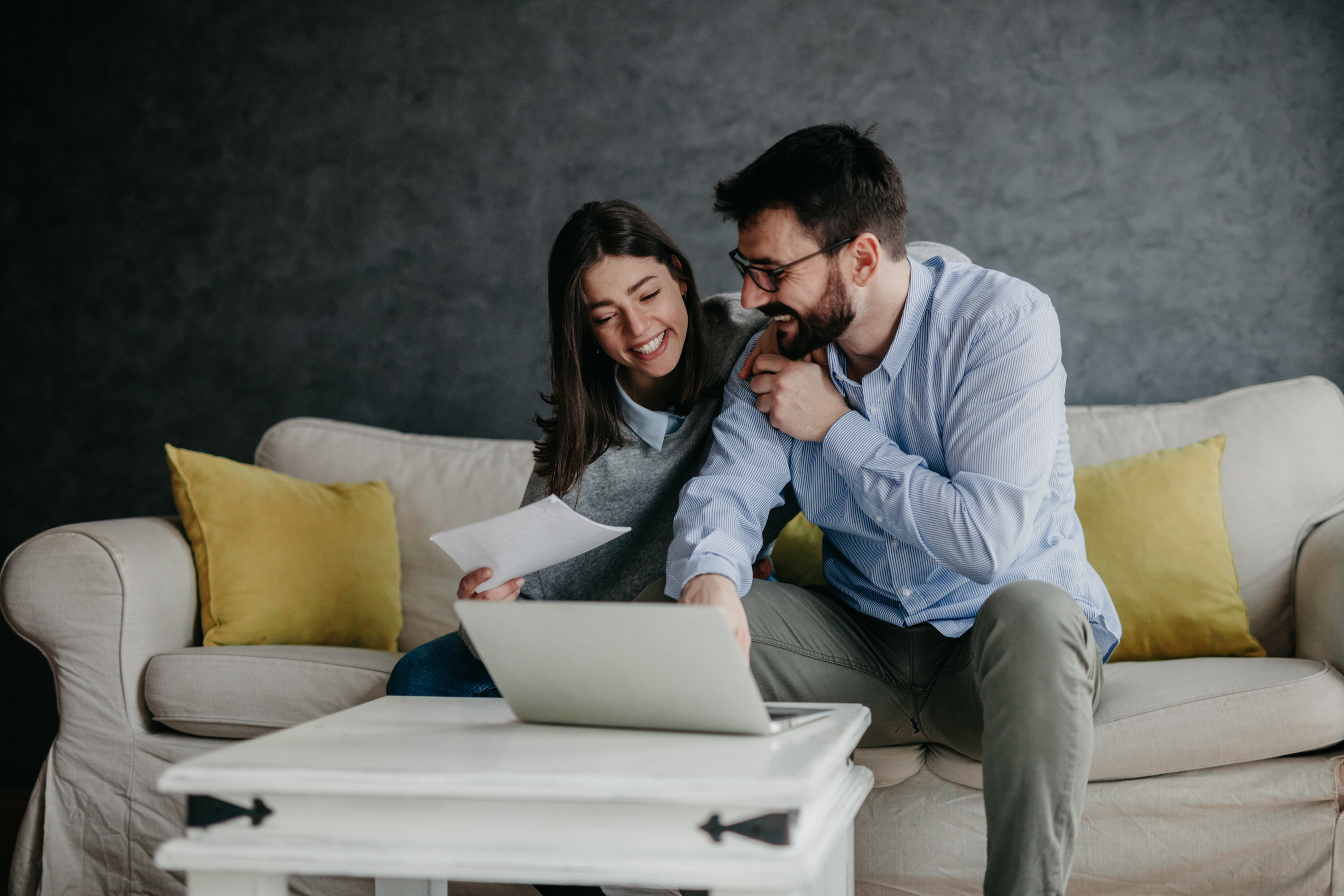 A couple smiles while planning their wedding together on their laptop