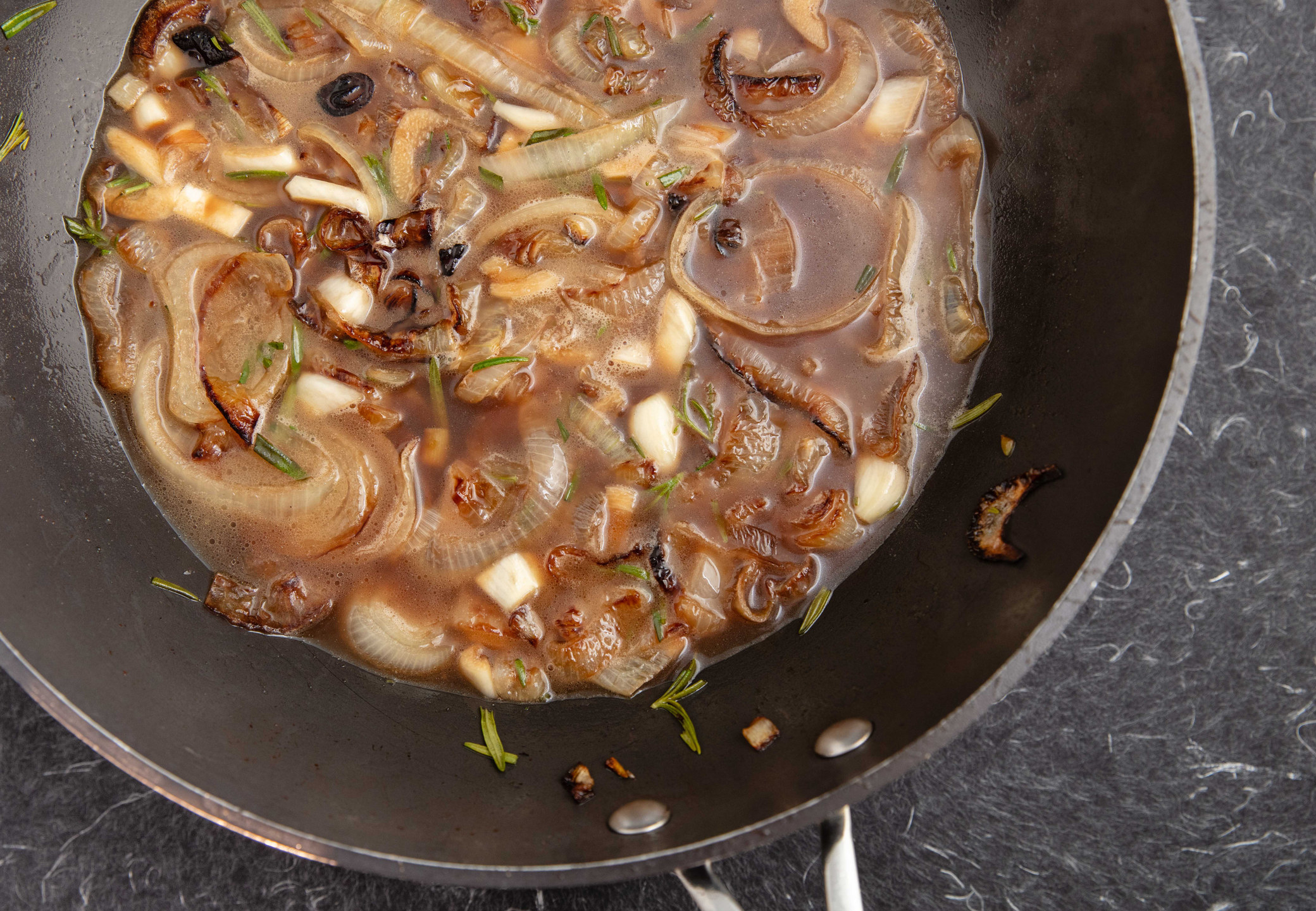 Caramelized onions in broth in a skillet.