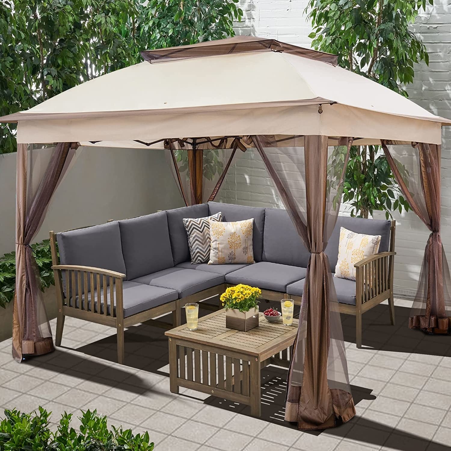 The gazebo outside with a couch and table underneath it and greenery around it