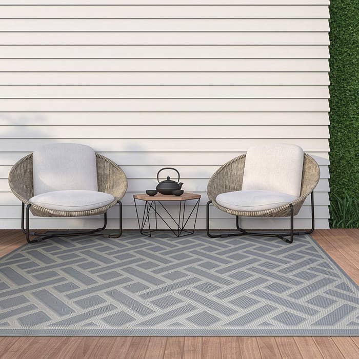 Two chairs, a side table, and the rug on a wooden floor outside against a wall