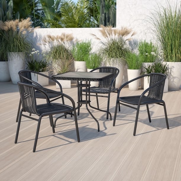 Four black outdoor chairs and a matching table on a patio with potted plants around