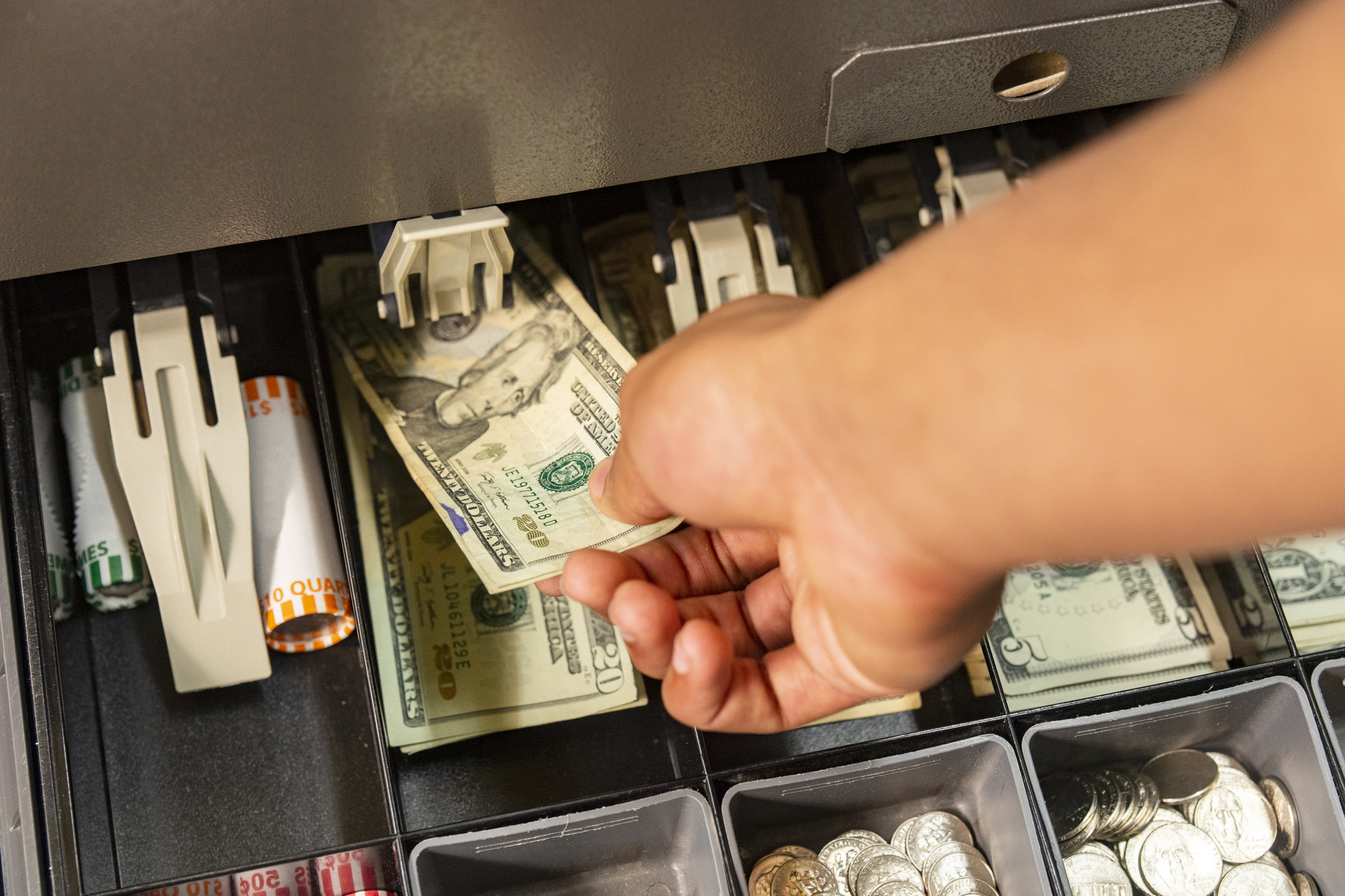 close-up of a person putting money in a till or cash draw.