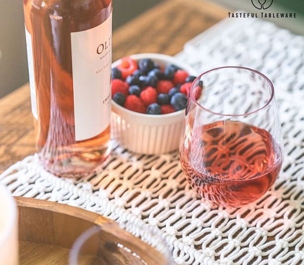Glass filled with pink wine, next to bottle and bowl with berries