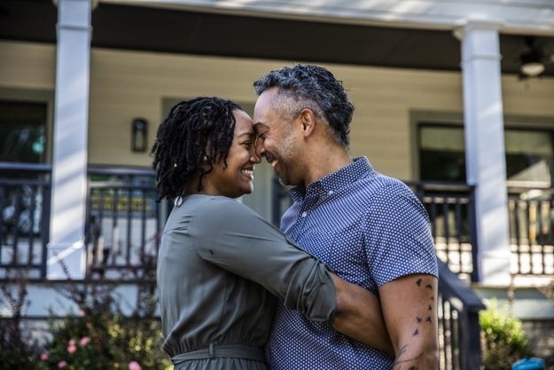A woman and man hug one another and smile in front of their house