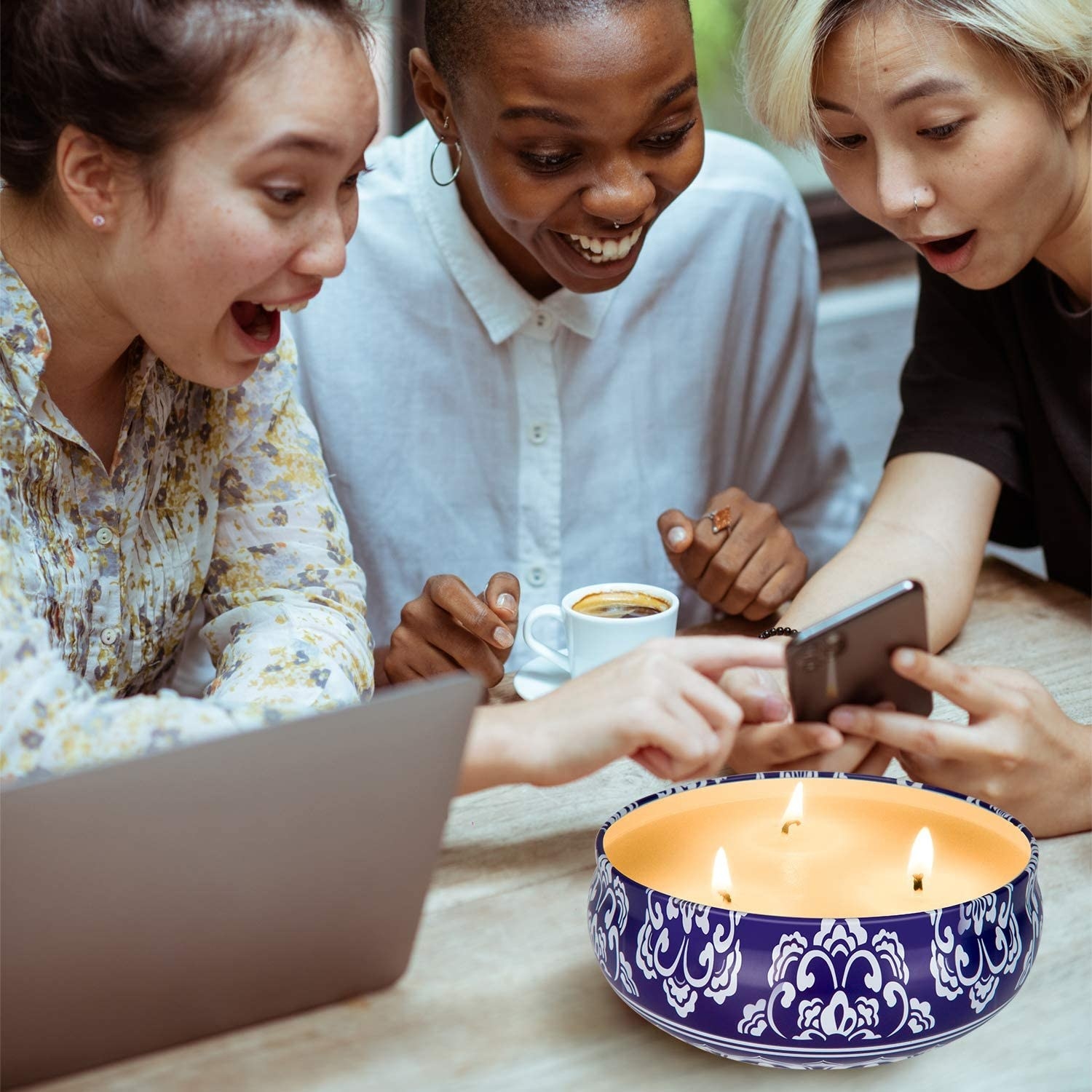 Three people smiling and looking at a phone with the candle beside them