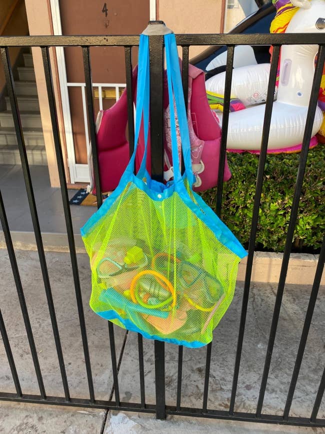 reviewer's mesh container holding toys hanging connected a fence