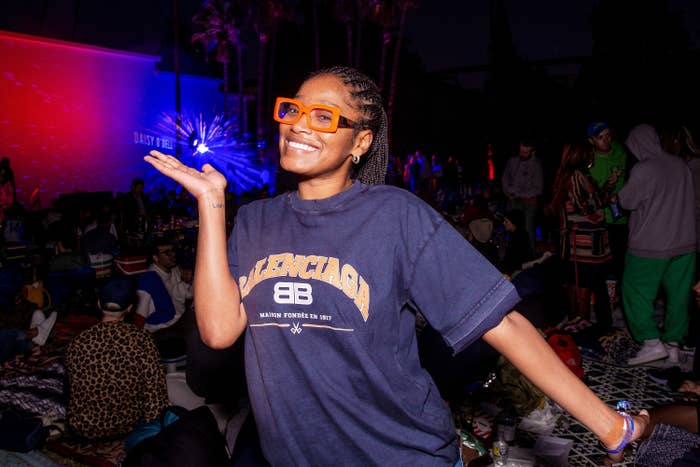 Keke Palmer poses in a blue shirt with orange sunglasses