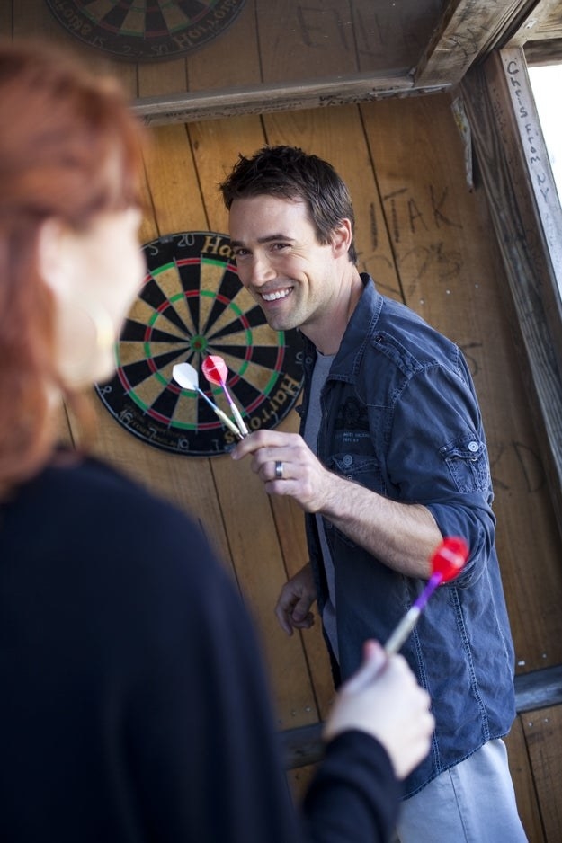A man smiles as he and a woman play darts together