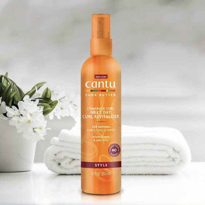 A bottle of curl enhancer with a flower bouquet and white folded towels