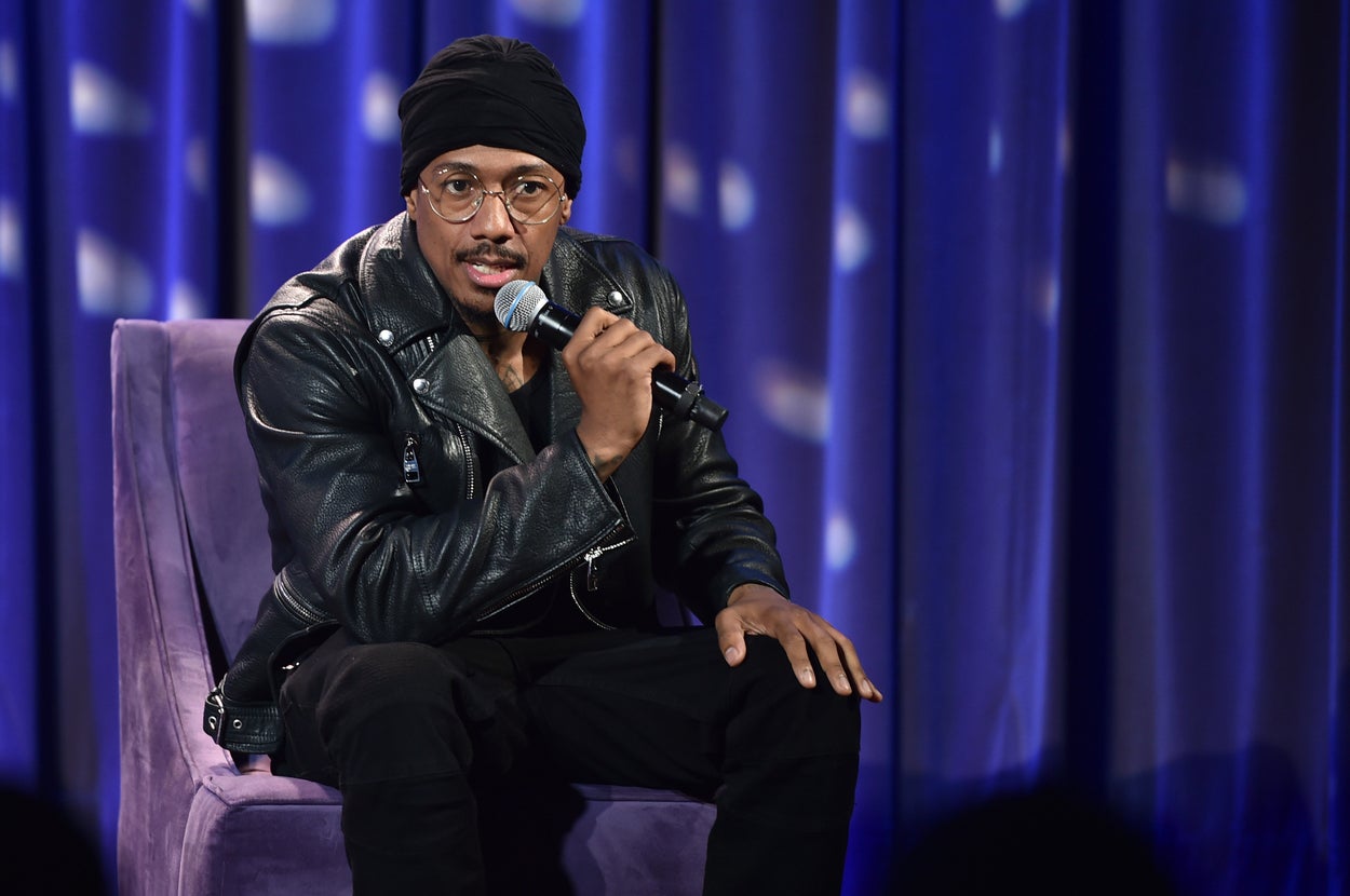 Nick Cannon speaks into a microphone wearing a black turban and a matching jacket