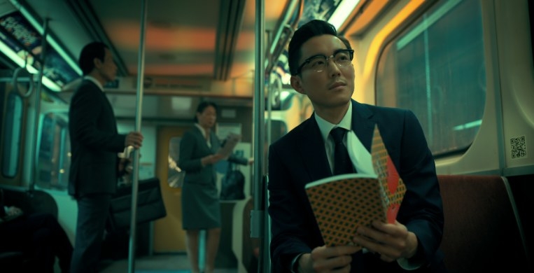 Sparrow Ben wears glasses and sits on a train reading a book