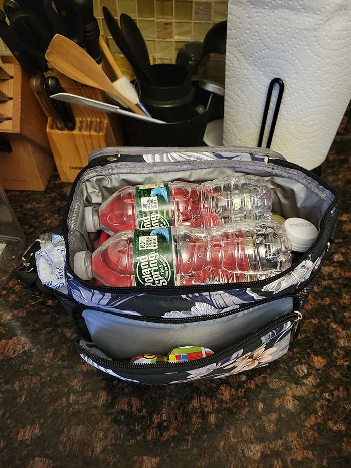 Reviewer&#x27;s photo of the floral lunchbox filled with water, food and snacks in outer pockets