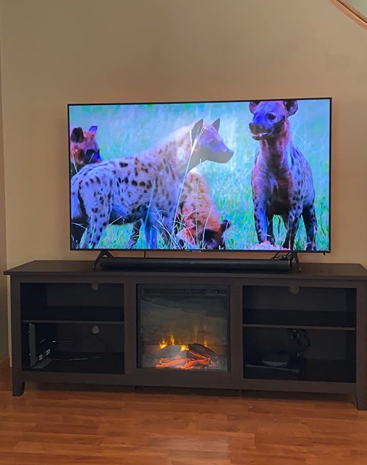 Reviewer&#x27;s photo of dark brown entertainment stand with fireplace on and supporting a flat screen tv showing a scene of hyenas