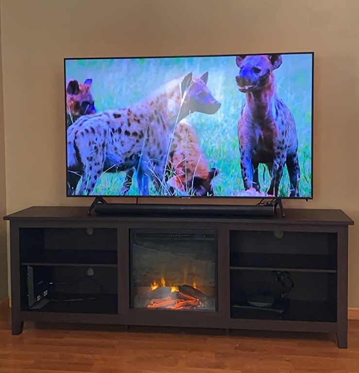 Reviewer&#x27;s photo of dark brown entertainment stand with fireplace on and supporting a flat screen tv showing a scene of hyenas