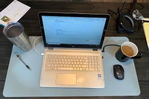 Reviewer pic of the rectangle desk mat in blue with laptop, coffee, mouse and pen on it 