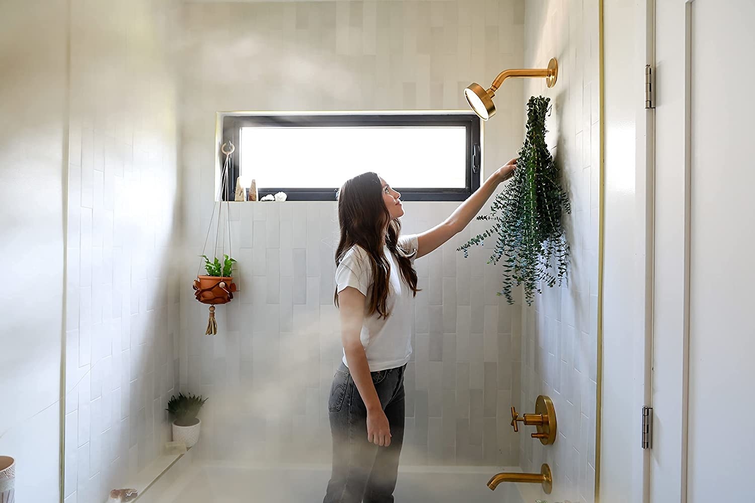person inside shower hanging up large bundle of eucalyptus