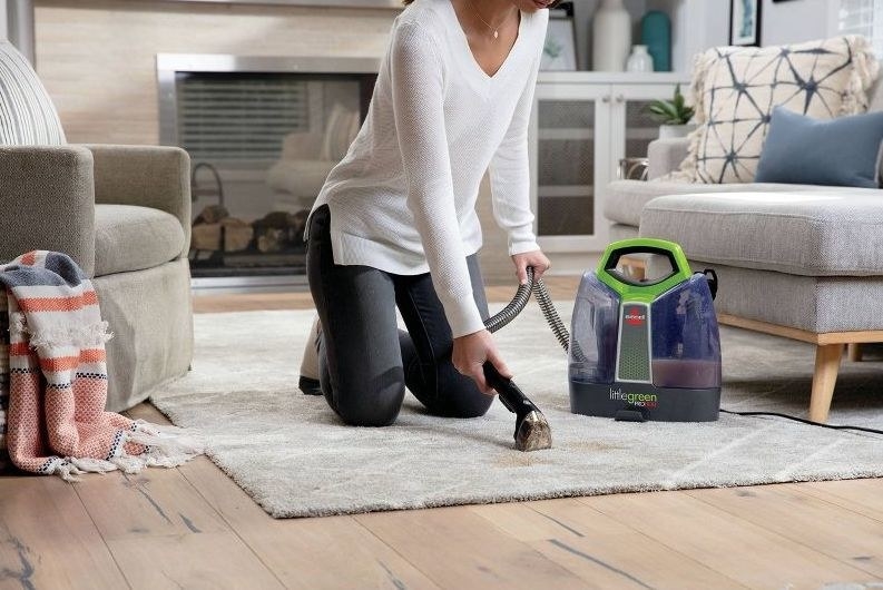 A person uses the little green vacuum on a rug