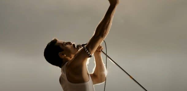 Rami Malek as Freddie Mercury, leaning back with his right arm raised high and his left arm holding a microphone to his mouth, which is open mid-song