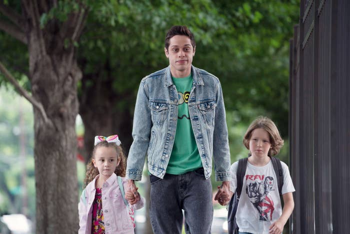Pete walking down the street wearing a denim jacket, T-shirt, and jeans and holding the hands of two children