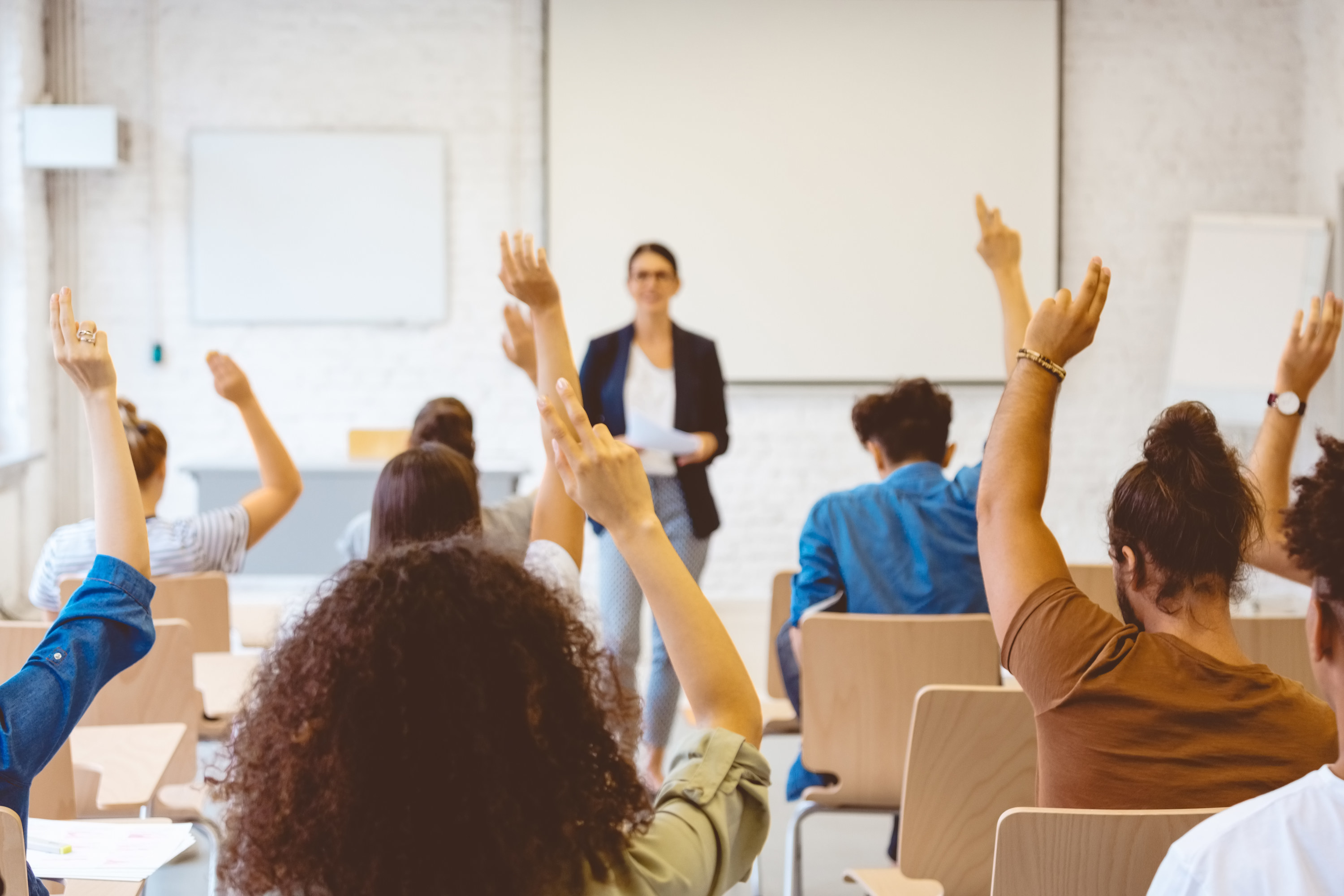 male and female students raising hands in classroom