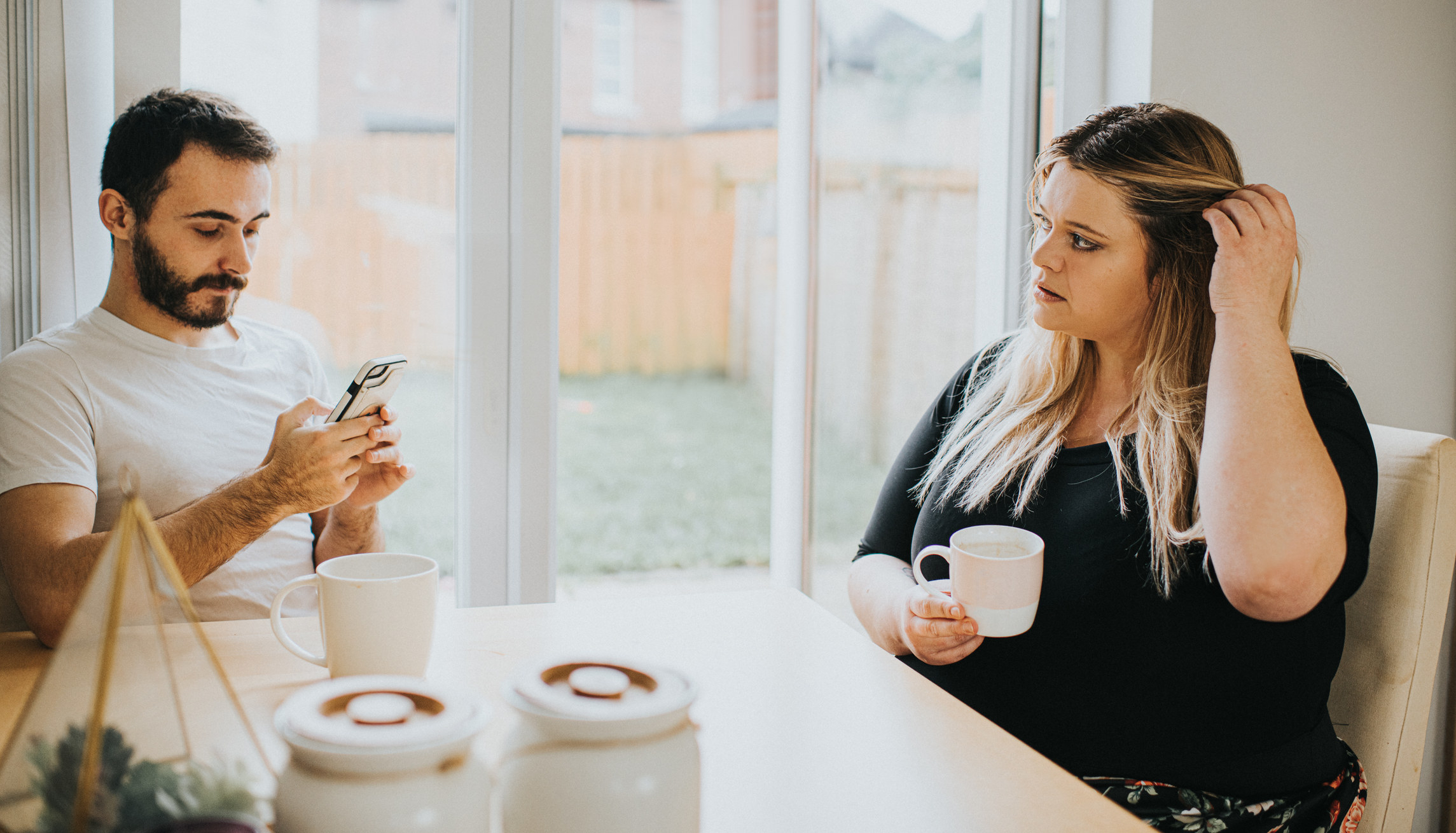 A man on his phone and a woman holding a coffee at the table