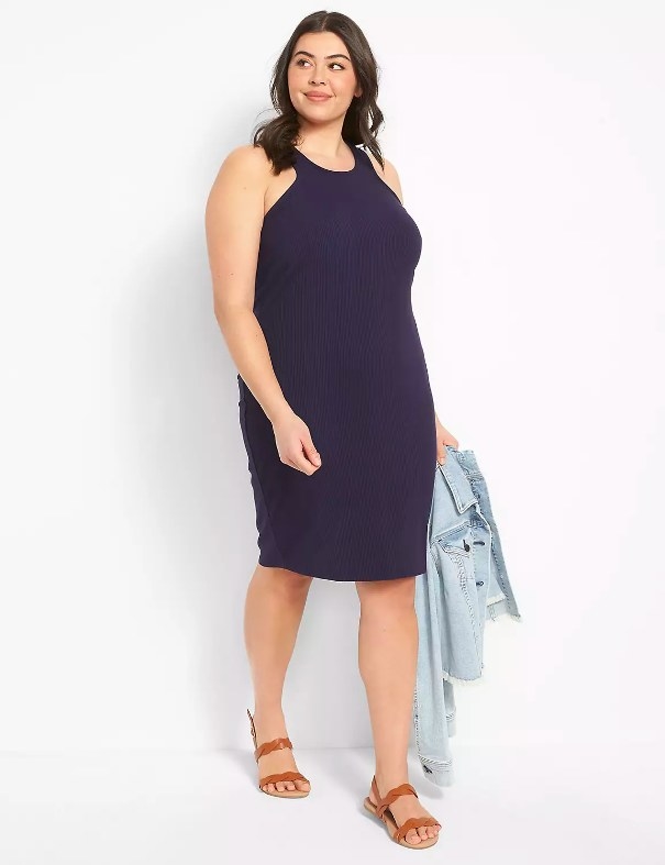 Model wearing navy dress with sandals holding a denim jacket