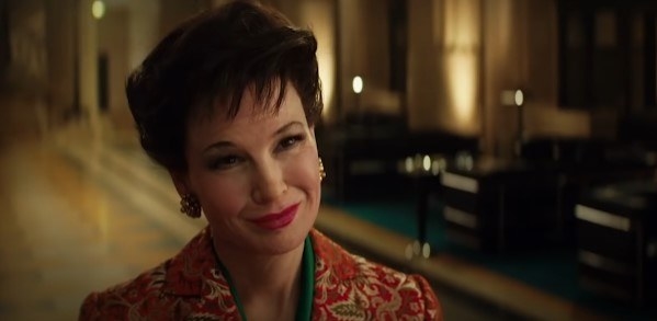 Renée Zellweger as Judy, smiling while wearing a red jacket with a gold floral pattern and a green blouse beneath