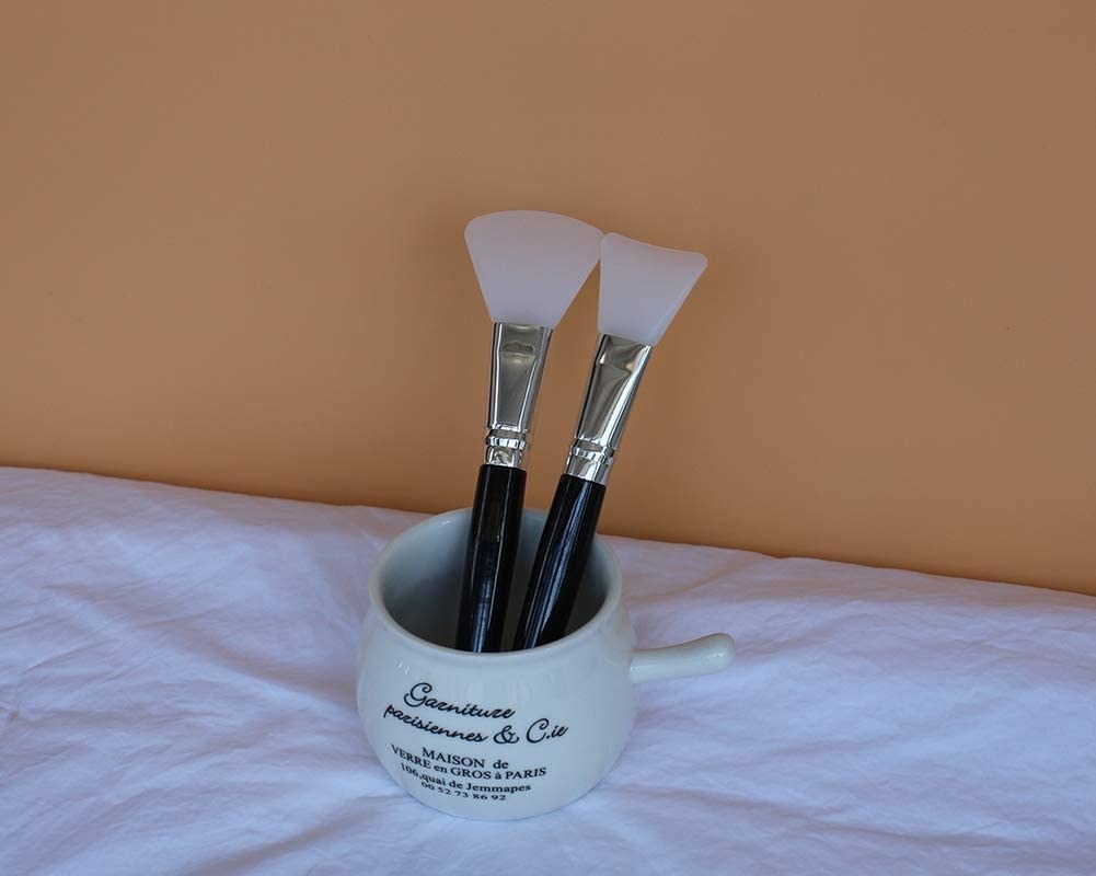 The brushes in a ceramic container on a bed